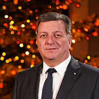 Porträt von Staatsminister Christian Bernreiter. Im Hintergrund ist ein beleuchteter Weihnachtsbaum zu sehen. © StMB