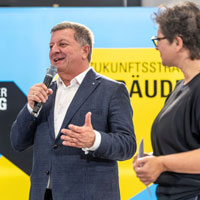 Staatsminister Bernreiter begrüßt die Teilnehmerinnen und Teilnehmer gemeinsam mit Moderatorin Eva Herrmann